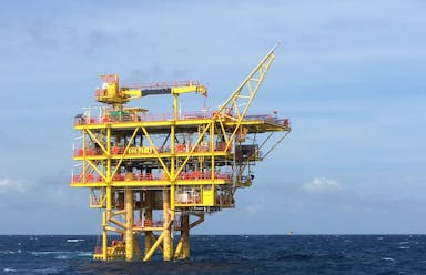 A yellow oil rig in the middle of the dark blue sea with a light blue sky in the background