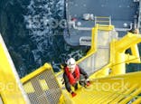 Man climbing up a yellow ladder on an oil rig, dark sea in the background