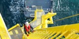 Man climbing up a yellow ladder on an oil rig, dark sea in the background